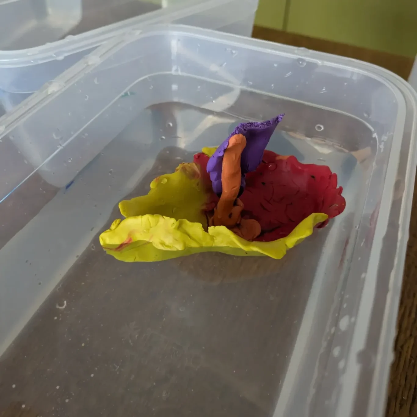 Die Magie des Auftriebs Bunte, aus Knetmasse geformte Blume schwimmt in klarem Wasser.