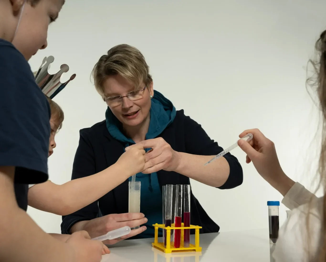 Eine Frau zeigt Kindern, wie man mit Reagenzgläsern experimentiert.