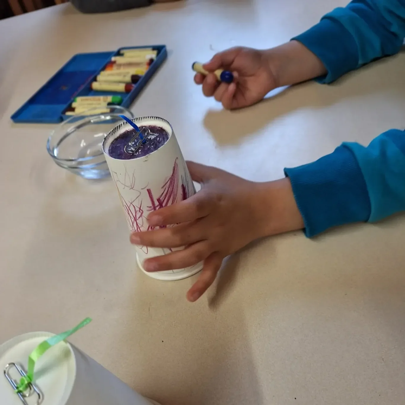Kreischbecher Ein Kind hält einen Becher mit einem Strohhalm, während es auf den Tisch schaut.